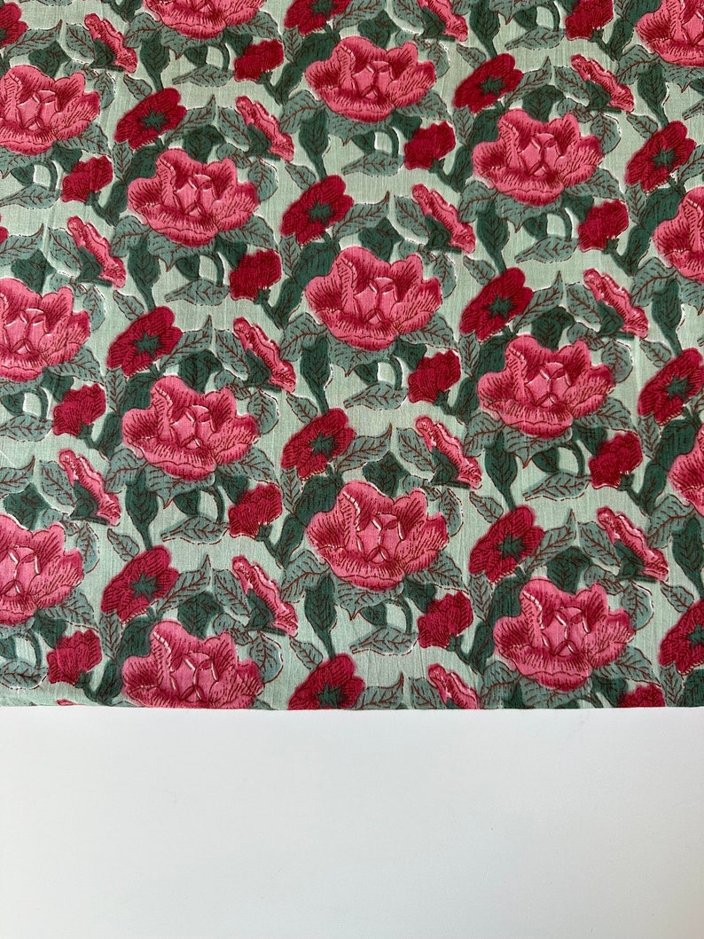 May include: A green fabric with a pink floral pattern. The fabric is covered in a repeating pattern of pink flowers with green leaves.