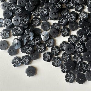 May include: A collection of black plastic buttons with a flower design. The buttons have two holes and a shiny finish.