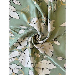 May include: A green fabric with a white floral pattern. The fabric has a silky texture and is perfect for crafting projects.