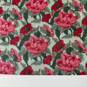 May include: A green fabric with a pink floral pattern. The fabric is covered in pink flowers with green leaves.