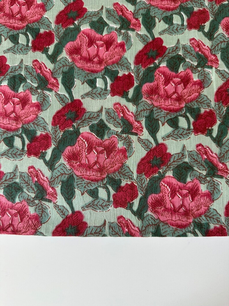 May include: A green fabric with a pink floral pattern. The fabric is covered in pink flowers with green leaves.