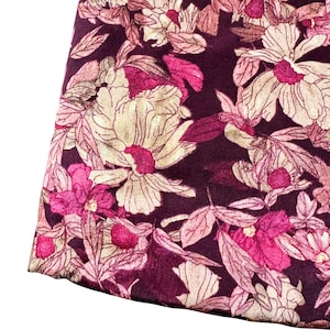 Könnte beinhalten: Nahaufnahme eines Stoffes mit floralem Muster. Das Design zeigt große, stilisierte Blumen in Creme-, Rosa- und Magentatönen auf einem tief burgunderfarbenen Hintergrund. Der Stoff hat ein weiches, strukturiertes Aussehen.