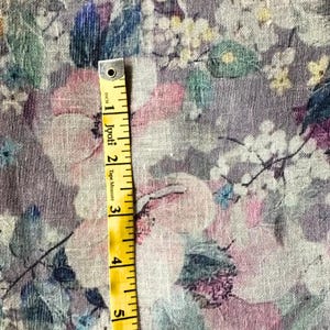 May include: Floral fabric with a watercolor effect in shades of pink, purple, blue, and green. A yellow tape measure, marked in inches, is placed over the fabric. The tape measure reads "Jyoti Tape Measure".