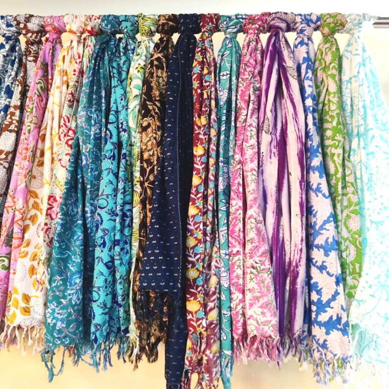May include: A collection of colorful scarves with floral patterns hanging on a rack. The scarves are made of cotton and have a variety of colors, including blue, green, pink, purple, and red.