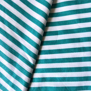 May include: Close-up of a fabric with a repeating pattern of teal and white stripes. The stripes run diagonally across the fabric, creating a visually appealing design. The fabric appears to be cotton or a similar material.