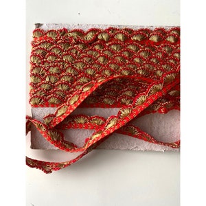May include: Red and gold trim with a scalloped edge. The trim is made of a woven fabric with a repeating pattern of small, fan-shaped designs.