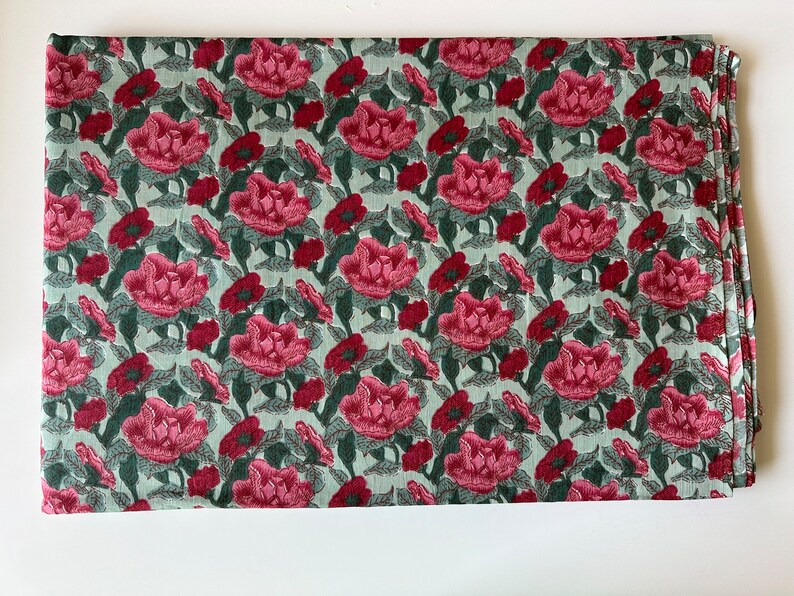 May include: A green fabric with a repeating pattern of pink flowers and green leaves.