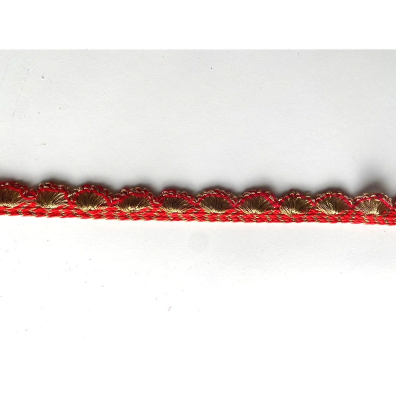 May include: Red and gold trim with a scalloped edge. The trim is made of a woven fabric with a textured surface.