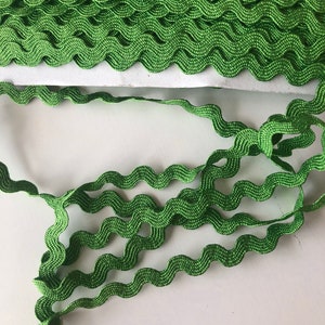 May include: A length of green wavy ribbon, a decorative trim with a zigzag edge. The ribbon is a vibrant shade of green. The image shows a close-up of the ribbon, highlighting its texture and design. The ribbon is likely used for crafting, sewing, or embellishing various projects.