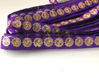 May include: Purple fabric trim with gold sequins in a flower shape.