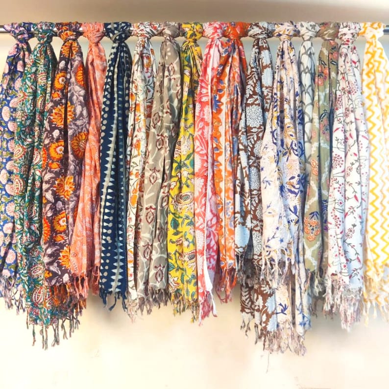 May include: A collection of colorful scarves with floral patterns. The scarves are made of cotton and have a fringed edge.