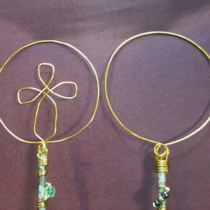 May include: A pair of gold hoop earrings with a dangling cross charm on one earring and a plain dangle on the other. The charms are made of gold wire and have a beaded detail.