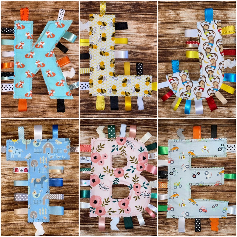 May include: A set of five fabric alphabet letters with colorful ribbon tails. The letters are K, L, B, and E. The fabric patterns include foxes, bees, flowers, farm animals, and trucks.