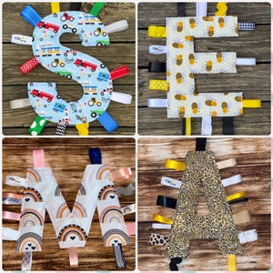 May include: Four fabric baby toys in the shape of the letters S, E, M, and A. Each letter is made of a different fabric and has colorful ribbons attached. The letters are arranged in a grid on a wooden surface.