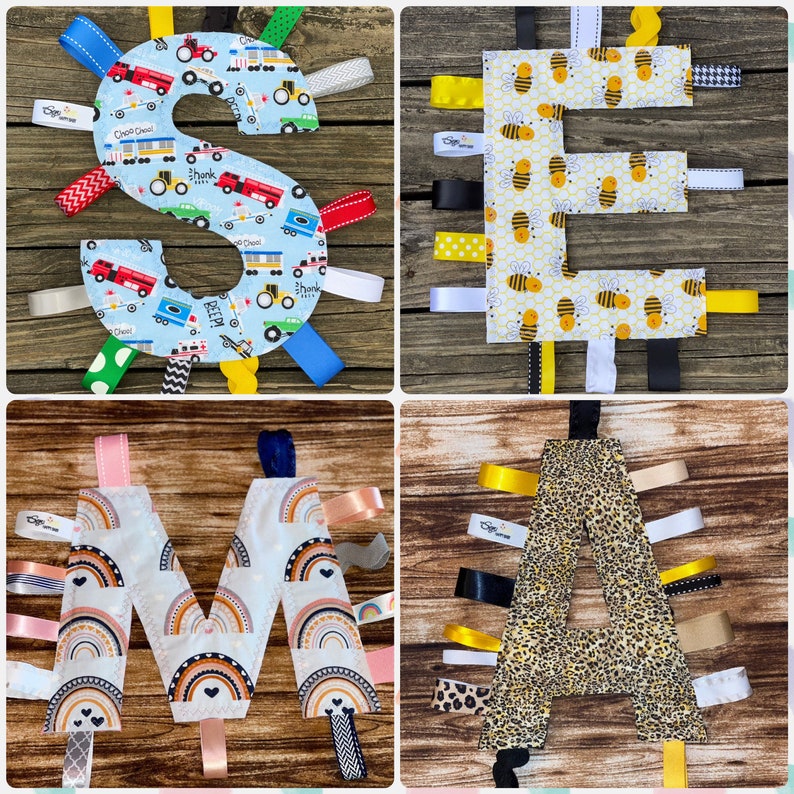May include: Four fabric baby toys in the shape of the letters S, E, M, and A. Each letter is made of a different fabric and has colorful ribbons attached. The letters are arranged in a grid on a wooden surface.