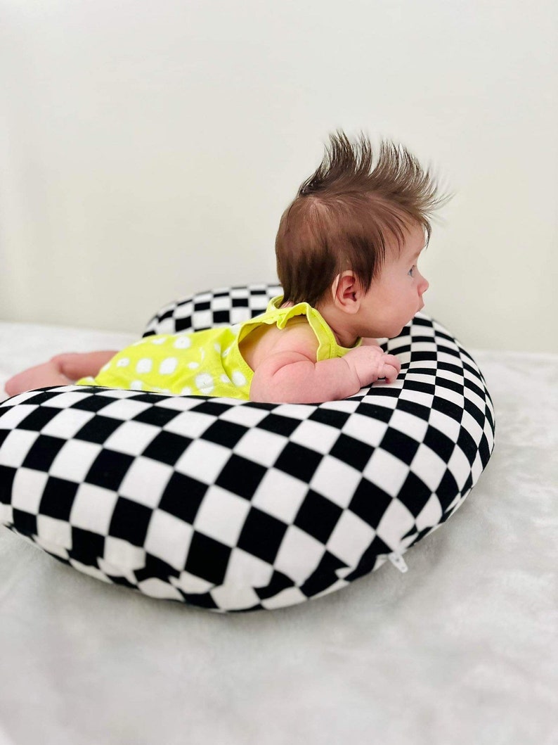 Pu&ograve; includere: Un bambino con un body verde a pois bianchi giace a pancia in gi&ugrave; su un cuscino a scacchi neri e bianchi.
