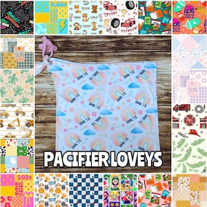 May include: A baby pacifier lovey with a rainbow and cloud pattern, personalized with the name "Daniel 318". The lovey is attached to a pink pacifier clip. The text "PACIFIER LOVEYS" is displayed.
