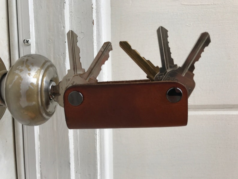 May include: A brown leather key holder with silver metal accents and multiple keys attached. The key holder is attached to a door knob.