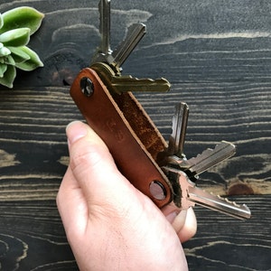 May include: A brown leather key holder with a metal clasp and a set of keys attached. The key holder has the initials "J.S." embossed on the front.