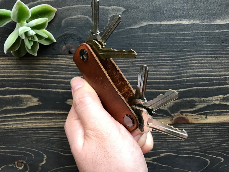 May include: A brown leather key holder with a metal clasp and a set of keys attached. The key holder has the initials "J.S." embossed on the front.
