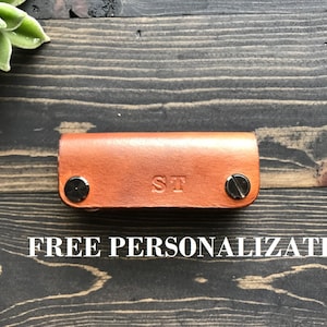 May include: A brown leather key holder with silver rivets and the initials "ST" embossed on the front.  FREE PERSONALIZATION is written in white text below the key holder.