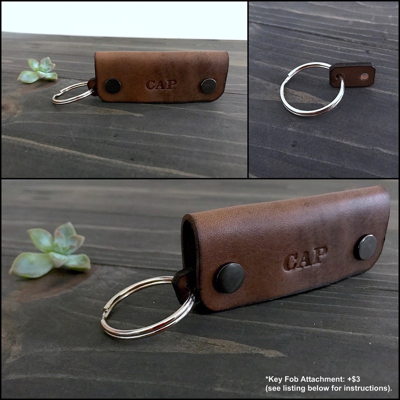 May include: Brown leather key fob with the name "CAP" embossed on it. The fob has two metal snaps and a silver key ring.