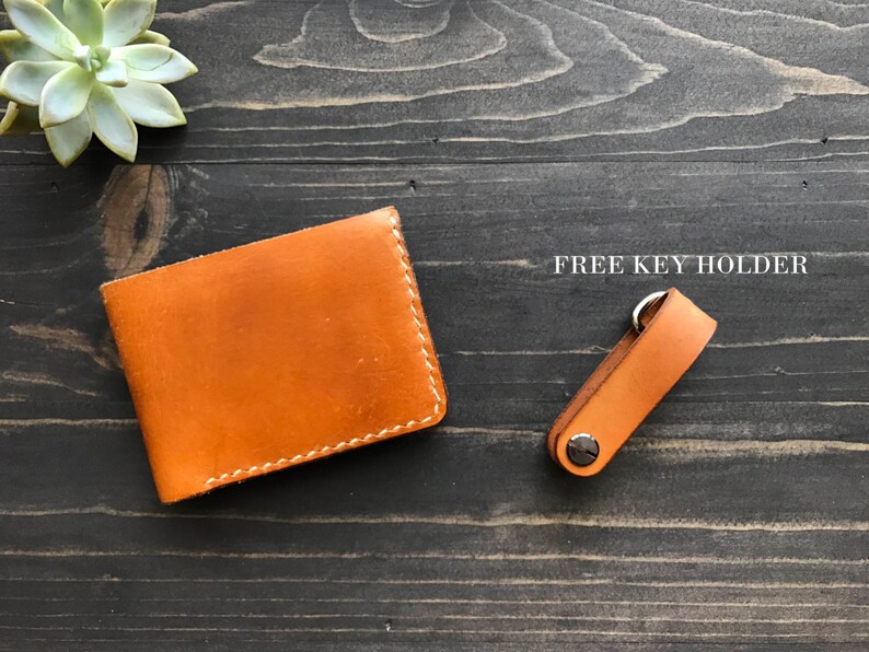 May include: A brown leather wallet with white stitching and a matching brown leather key holder with a silver ring. "FREE KEY HOLDER" is written in white text on a black background.