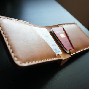 May include: A brown leather wallet with a stitched edge, open to reveal two credit cards inside. The wallet is on a dark surface.
