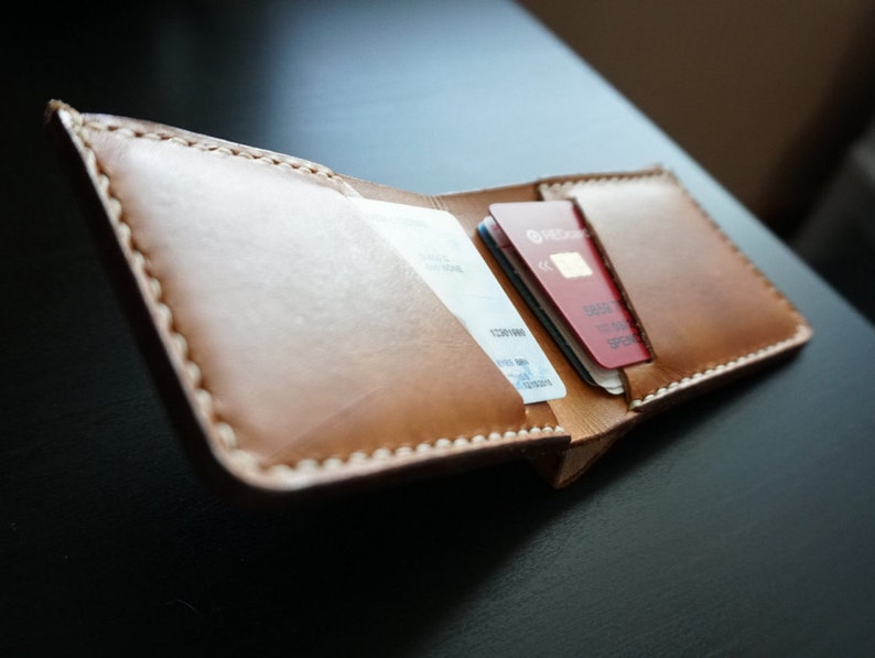 May include: A brown leather wallet with a stitched edge, open to reveal two credit cards inside. The wallet is on a dark surface.