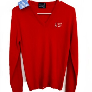 May include: A red V-neck sweater with long sleeves, hanging on a hanger. The sweater has the text "Johnnie Walker Red" embroidered on the chest, along with a logo. A tag is attached to the sweater.