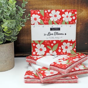 May include: A stack of red and white fabric squares with a floral print. The fabric squares are labelled "Love Blooms" by "2" Little Boutique.