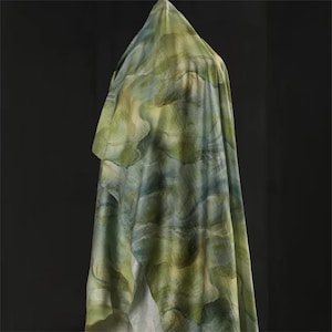 May include: A draped fabric with a watercolor-like pattern in shades of green, blue, and yellow. The fabric is draped over an unseen form, creating soft folds and a flowing appearance. The overall effect is artistic and organic.