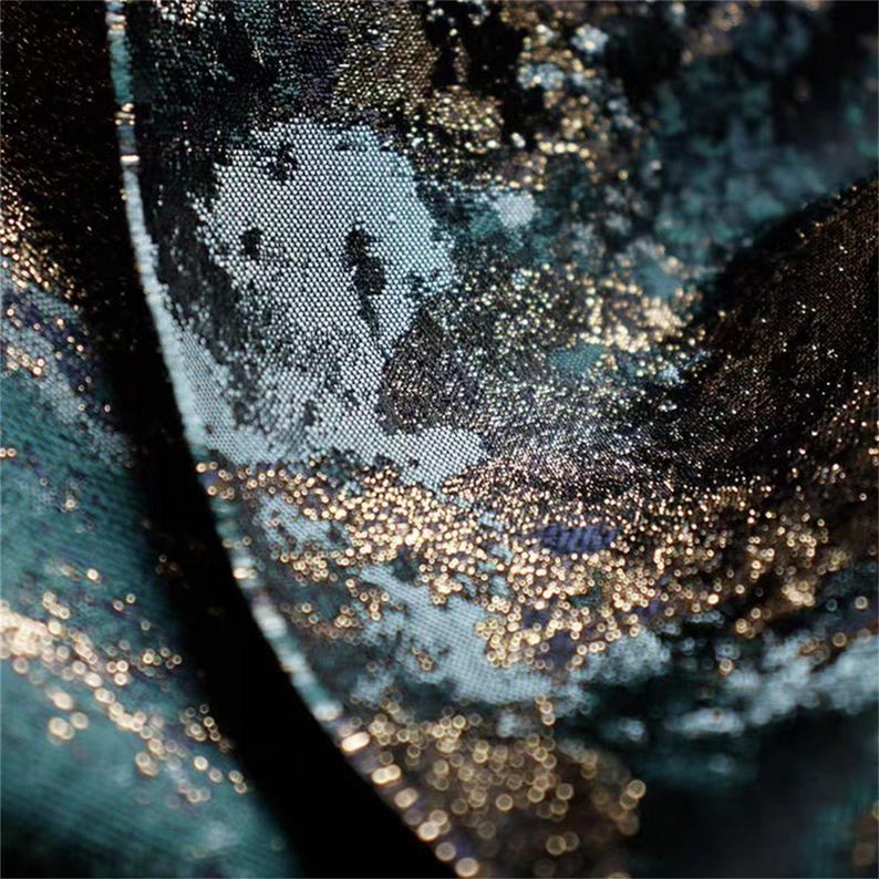 May include: Close-up of a textured fabric with a teal and black base, overlaid with shimmering gold accents. The fabric has a subtle, grid-like pattern, creating a luxurious and elegant appearance. The gold elements add a touch of sparkle and depth.