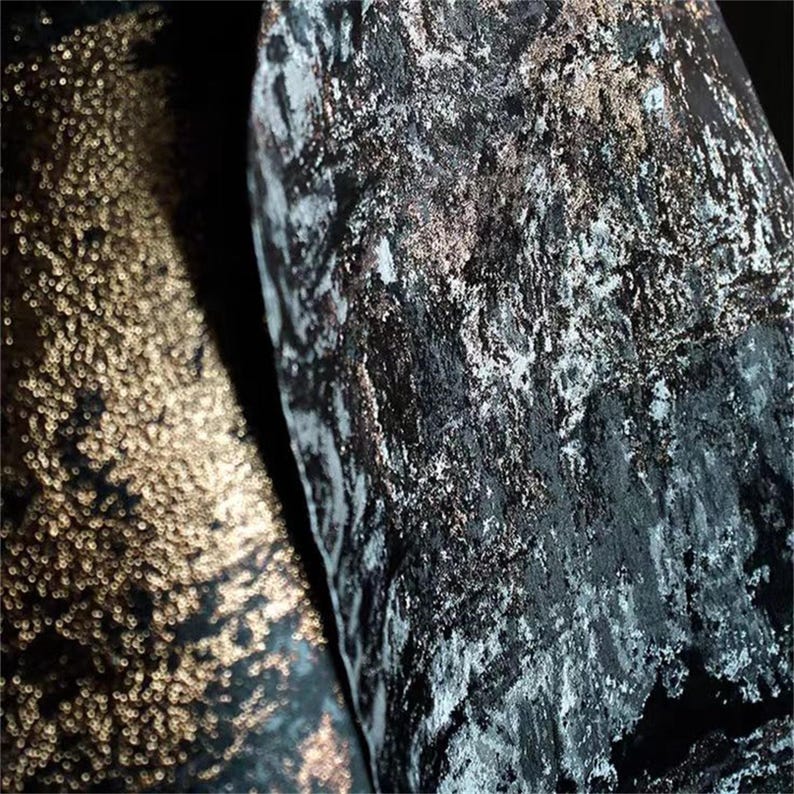 May include: Close-up of two textured fabrics. One fabric is a dark, shimmering black with silver and gold accents. The other fabric is a gold, textured material with a bubbly appearance. The fabrics are side by side.
