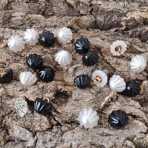 May include: A collection of small, round buttons featuring a ridged, shell-like texture. The buttons are finished in alternating glossy black and pearlescent white colors, each equipped with a small gold-toned metal shank loop on the underside.