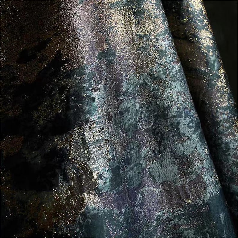 May include: Close-up of a textured fabric with a dark, abstract design. The fabric features a blend of deep blues, greens, and purples, accented with shimmering gold flecks. The overall effect is a rich, artistic textile.