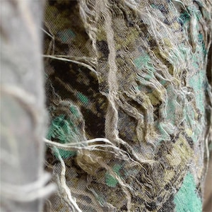 Può includere: Primo piano di un tessuto strutturato con un motivo verde, marrone e giallo. Il tessuto ha un aspetto invecchiato con bordi sfilacciati e fili bianchi. L'effetto complessivo è una miscela di colori e trame.