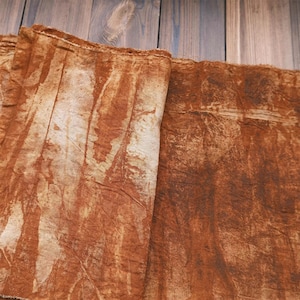 Puede incluir: Primer plano de tela doblada y texturizada en tonos marrones y beige. La tela tiene un aspecto arrugado con áreas más claras que crean un efecto veteado. El material parece ser natural, posiblemente lino o algodón.