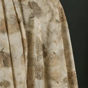 May include: A piece of fabric featuring a botanical print with various leaf shapes in shades of brown, tan, and cream. The material has a soft, draped texture with visible folds and pleats, showcasing an organic, earth-toned pattern throughout.