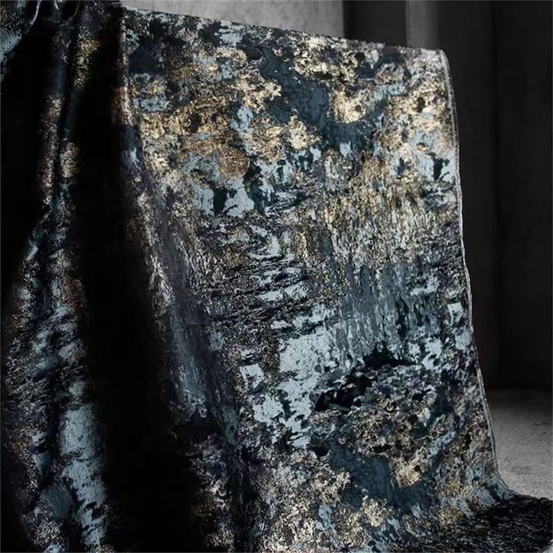 May include: Textile with a dark teal and black base, overlaid with gold metallic accents. The fabric has a textured, abstract pattern, creating a luxurious and artistic appearance. The material is draped over a surface, showcasing its flow and design.