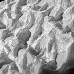 Op de afbeelding: Close-up van een grijze, getextureerde eierdoos. De doos heeft een gegoten, golvende oppervlakte met talrijke cirkelvormige openingen. Het materiaal lijkt gemaakt van gerecycled papier of karton, met een licht ruwe textuur.