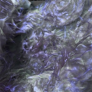 Puede incluir: Imagen abstracta de tela texturizada en capas en tonos morado, gris y blanco. La tela parece estar en capas y arrugada, con una textura suave y plumosa. El efecto general es etéreo y onírico.