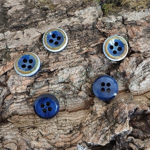 May include: Five circular buttons with four holes each. Three buttons feature a dark blue center with a light brown outer ring and a silver edge. Two buttons are solid dark blue with a smooth, glossy finish and a dark outer rim.