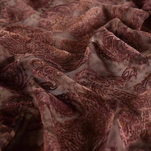 Peut inclure: Gros plan sur un tissu transparent avec un motif cachemire. Le tissu est d'un bordeaux profond avec un fond plus clair, presque transparent. Le motif cachemire est en relief et texturé, créant une sensation de profondeur et de luxe.