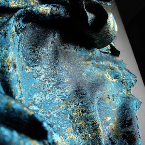 May include: A piece of fabric featuring a deep teal and black base with a metallic gold foil overlay. The material has a textured, crinkled appearance with folds that create shadows and highlights across the surface of the shimmering textile.
