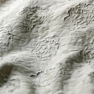 Può includere: Primo piano di un tessuto strutturato con un motivo floreale. Il tessuto è di un colore chiaro e neutro, forse bianco sporco o grigio chiaro. Il motivo floreale in rilievo aggiunge profondità e interesse visivo al tessuto.