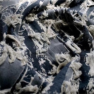 May include: Close-up of a textured fabric with a distressed design. The fabric features a dark blue and gray color palette with white accents and frayed edges, creating a vintage or bohemian aesthetic. The fabric is likely used for home decor or apparel.