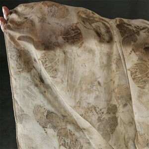 May include: A lightweight, semi-sheer scarf featuring an all-over botanical print with various leaf shapes in shades of muted brown, tan, and cream. The fabric displays a soft, organic texture with visible leaf vein details across the entire surface.