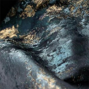 May include: Close-up of a textured fabric with a dark teal and gold color scheme. The fabric has a marbled appearance with gold flecks and a subtle sheen. The folds and textures create a sense of depth and movement.