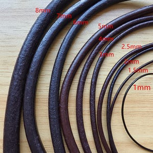 Puede incluir: Primer plano de varios cordones de cuero marrón oscuro de diferentes grosores, que van de 1 mm a 8 mm. Los cordones están dispuestos uno al lado del otro, mostrando los diferentes tamaños. La imagen está tomada sobre una superficie de madera marrón claro.